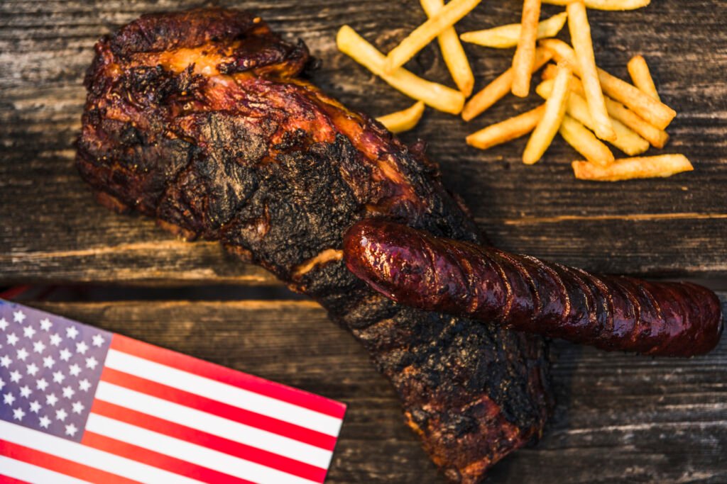 Slow smoked American BBQ ribs and sausage served with fries and US flag on rustic wooden table